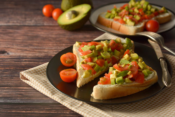 Healthy toast with avocado, cherry tomatoes and cheese on a plate. Wooden table.