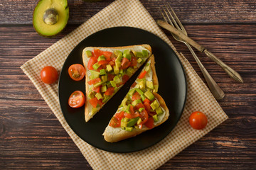Healthy toast with avocado, cherry tomatoes and cheese on a plate. Wooden table.