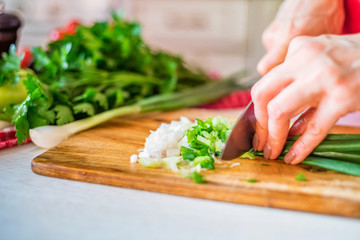 Obraz na płótnie Canvas Female hand with knife cuts green leek in kitchen. Cooking vegetables