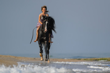 Portrait of a beautiful blond girl galloping on horseback, dissecting waves on the sea beach