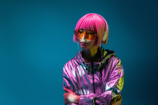 Young Asian woman with stylish pink haircut and sparkly silver jacket standing and listening music