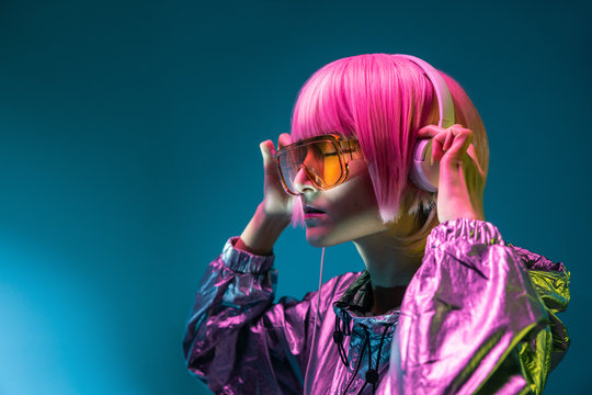 Young Asian woman with stylish pink haircut and sparkly silver jacket standing and listening music