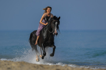 Portrait of a beautiful blond girl galloping on horseback, dissecting waves on the sea beach