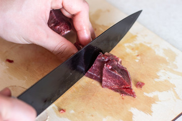 A black knife cuts the meat into pieces. cut the meat into pieces. The mistress of finely cut meat. Cutting meat with a black knife
