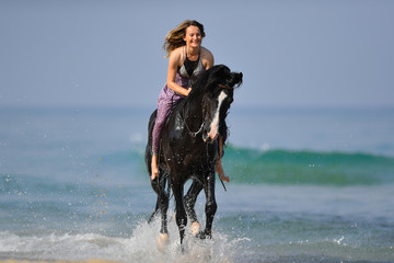 Portrait of a beautiful blond girl galloping on horseback, dissecting waves on the sea beach