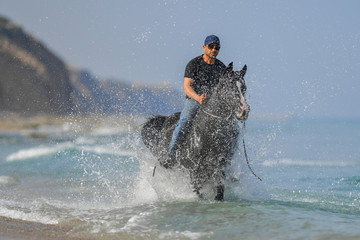 Fototapeta premium Portrait of a man galloping on horseback, dissecting waves on the sea beach