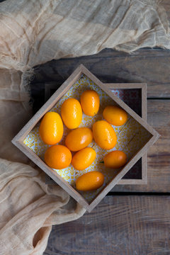 Composition of tropical kumquats placed in wooden boxes decorated by grey fabric on planks
