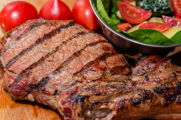 Close up freshly grilled bone steak on wood and fresh salad in bowl