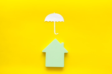 Insurance concept with house figure and umbrella on yellow background top view