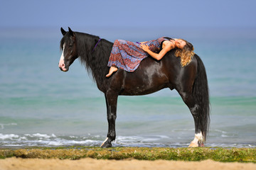 Fototapeta na wymiar Portrait of a beautiful blond girl run on the sand with her black horse on the Rishpon beach, Israelck horse on the Rishpon beach, Israel