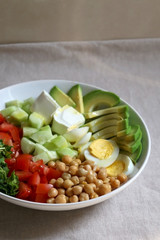 Lunch bowl with avocado, hard boiled egg, chickpea, feta cheese, cucumber, tomato and arugula. Selective focus.