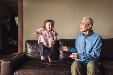 Granddaughter playing with her grandfather on sofa at home