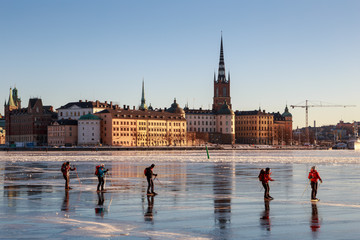 People are ice skating on frozen Riddarfjärden bay of lake Mälaren by Gamla Stan (Old Town) island, on a bright sunny and cold winter day with sub-zero temperature in Stockholm, Sweden.