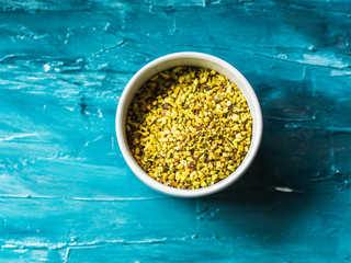 Chopped pistachio in bowl on green background. Ingredient