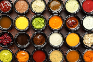 Top view closeup many different sauces bowls at brown textured background.