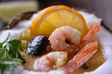 Soup tom yam in a coconut with shrimps and mushroom on a wooden table next to slice of lemon, macro