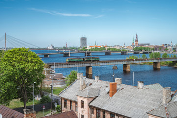 Fototapeta premium Panoramic view of Riga city covered in clouds. Iconic railroad bridge and old town panorama across the river Daugava. Picturesque scenery of historical architecture. National library of Latvia.
