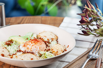 Healthy salad with baked chicken breast, poached egg, lettuce, cheese, avocado. Dieting food. Served salad in bowl on wooden table in cafe. Copy space
