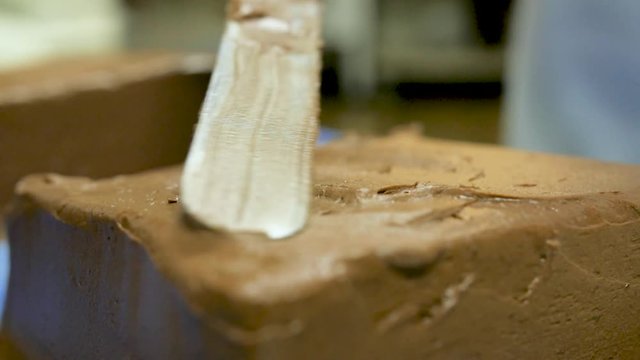 slow motion top frosting of chocolate cake close up. Chocolate cake being frosted back and forth to make a design on top. Baker uses a flat spatula.