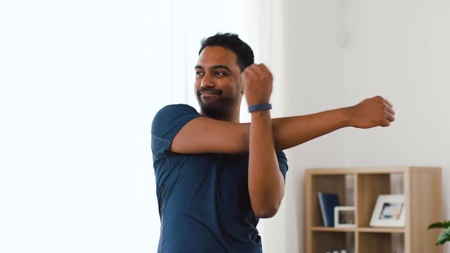 sport and healthy lifestyle concept - indian man with fitness tracker stretching body at home