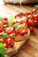 Traditional italian antipasto bruschetta appetizer with cherry tomatoes, cream cheese, basil leaves and balsamic vinegar on cutting board. Antipasti