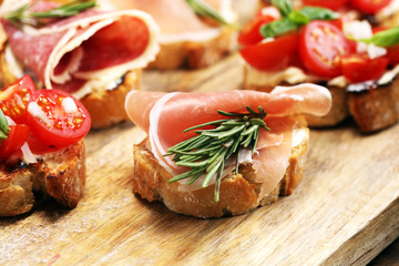 antipasto various appetizer. Cutting board with prosciutto, salami, cheese, bread and olives on dark wooden background