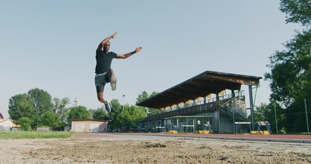 Slow motion close up of young african male athlete is performing a long jump on race track in athletics stadium in a sunny day.