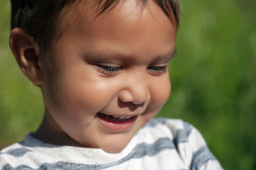 The cute face of a hispanic young boy smiling and looking thoughtful at something on a sunny day.