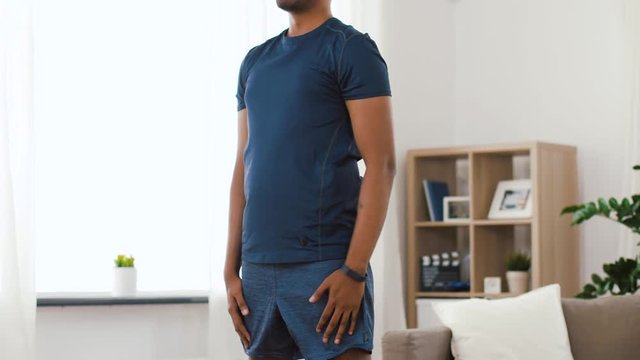 sport and healthy lifestyle concept - indian man with fitness tracker exercising and doing squats at home