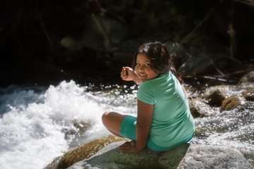 Young girl sitting on a rock next to river rapids during summer camp day trip.