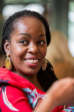 Portrait of smiling woman with cornrows wearing golden earrings and red top.,Oxfordshire