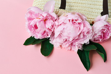 Pink peony flowers in summer woven straw bag on pink background.