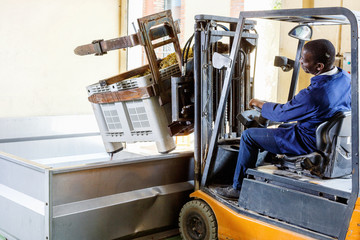 African American male worker controlling process of unloading grapes with forklift