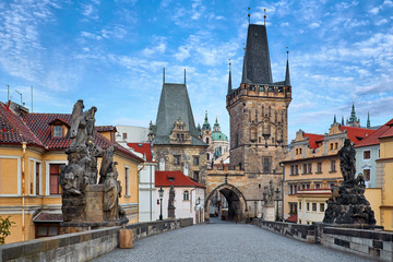 Fototapeta na wymiar Morning at Charles Bridge in Prague, Czech Republic. Solitary road with statues and paving stones. Antique medieval tower and arch of entrance to the old town Mala Strana district downtown.