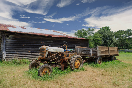An old rusty tractor by a weathered barn in a field
