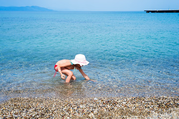 little girl in swimsuit collects pebbles in the sea. Summer vacation in Aegean Sea, Kos Island Greece