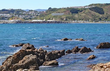 Fototapeta na wymiar Jagged rocks on the edge of Lyall Bay in Wellington, New Zealand. Airport buildings can just be seen in the background.