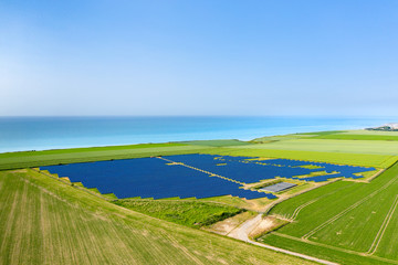 Un champ de panneaux solaires au milieux de champs de lin et de colza au bord de la mer
