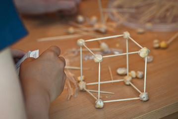 The atom model is made of supportive materials. Molecular grid of toothpicks and nuts. School scientific exhibition.