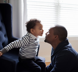 Side view of son kissing father while sitting on armchair at home