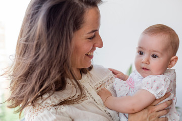 portrait of a beautiful baby girl and her mother at home by the window. Family concept indoors. Daytime and lifestyle