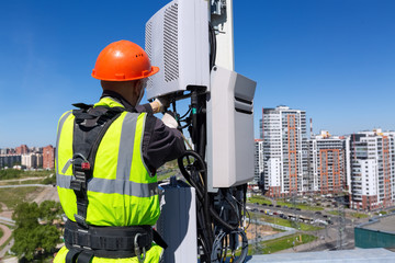 Telecommunication engineer in helmet and uniform installs telecomunication equipment in his hand...