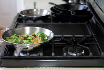 Stir fry vegetables cooking in a stainless steel pan on a natural gas stove.