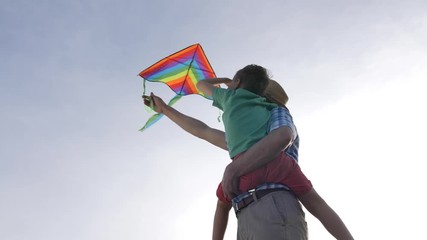 Low angle view of grandfather and grandson flying colorful kite and looking at bright blue sky. Elderly man teaching his little boy to fly kite whike enjoying joint leisure on sunny day