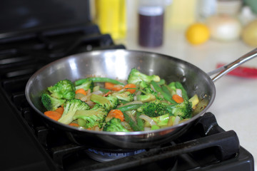 Stir fry vegetables cooking in a stainless steel pan on a natural gas stove.