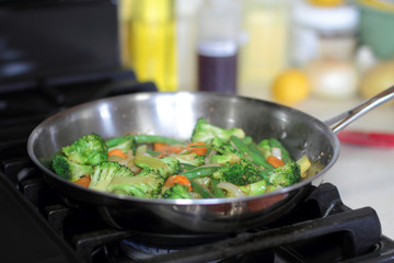 Stir fry vegetables cooking in a stainless steel pan on a natural gas stove.