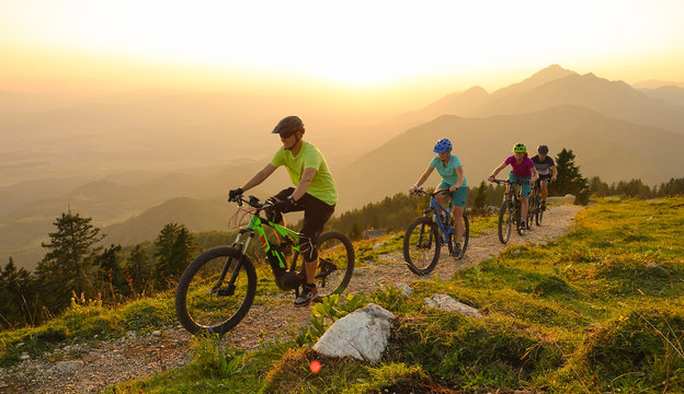 SUN FLARE Cheerful tourists ride electric bicycles up a mountain trail at sunset