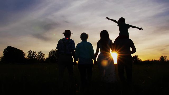 Silhouettes of three generation family walking holding each others hands among grass in meadow spending outside leisure together in country. Happy family enjoying beauty of sunset during walk outdoor