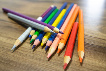  Colored pencils arranged on top of a table with woody texture. Colors of pencils blue, purple, pink, red, orange and silver.
