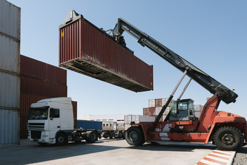 Crane lifting cargo container on truck on industrial site